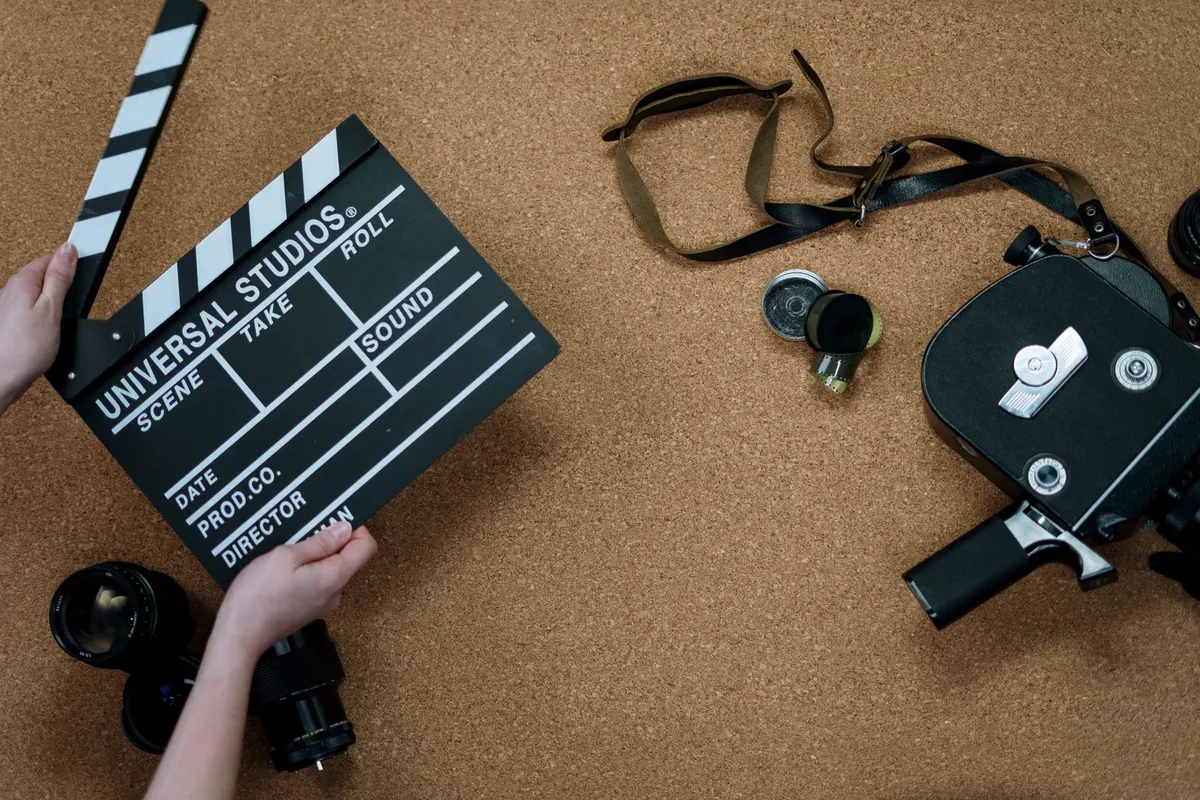 Top view of vintage film camera and clapperboard on cork background, evoking old cinema vibes.